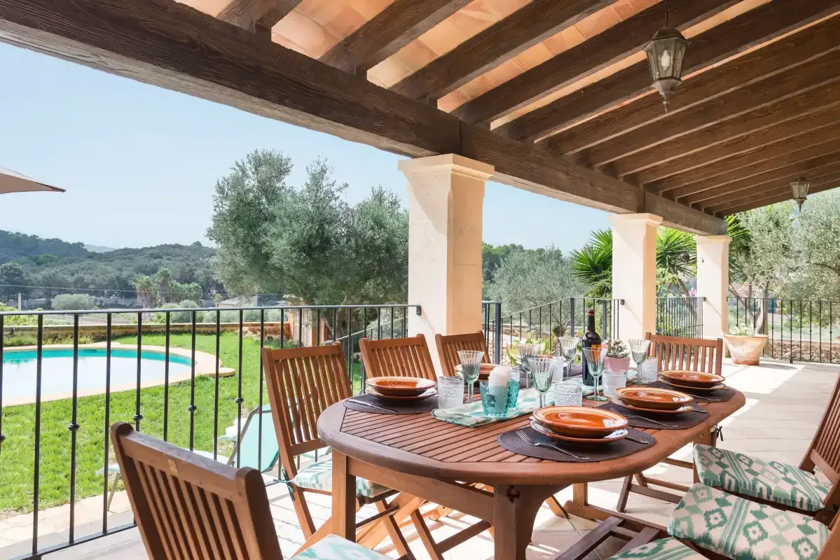 Una zona de comedor exterior cubierta ofrece vistas a una piscina y un paisaje verde.