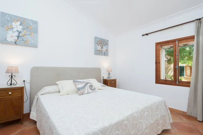 Un dormitorio con una cama bien tendida y una ventana con marco de madera.