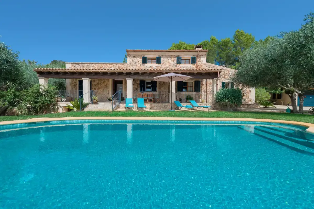 Una piscina frente a una casa de piedra con asientos al aire libre.