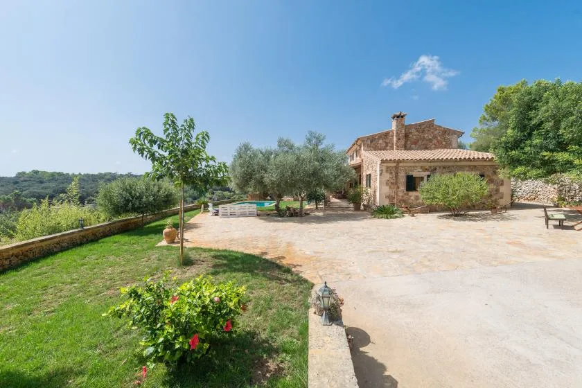 Una casa de piedra junto a una amplia terraza pavimentada y un jardín.