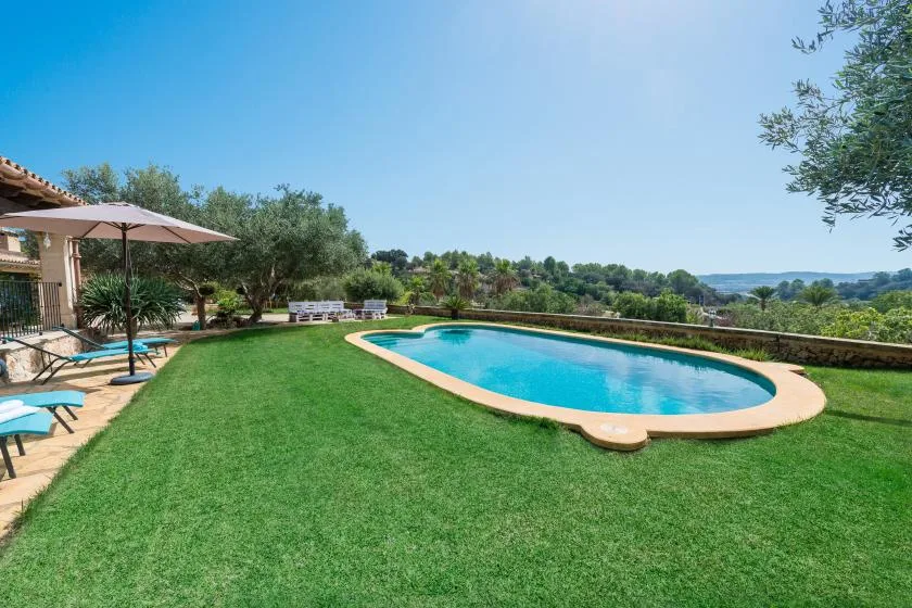 Una piscina al aire libre está en un jardín con césped junto a un patio.