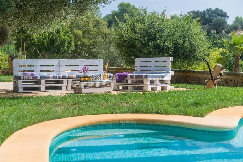 Una piscina al aire libre está junto a un jardín con césped y asientos de palés.