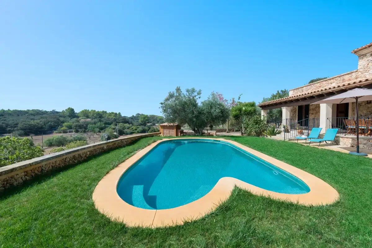 Una piscina está en un jardín con césped, junto a una casa y un patio.