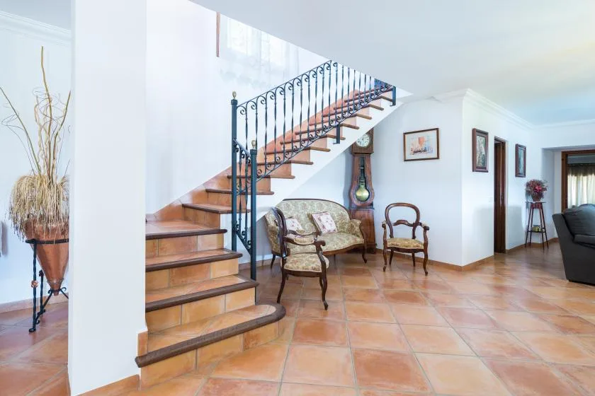 Un pasillo interior de baldosas con una escalera de madera y asientos debajo.