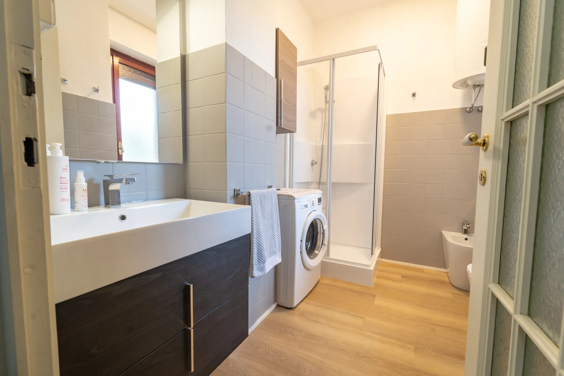 A bathroom with a sink, washing machine, and shower.