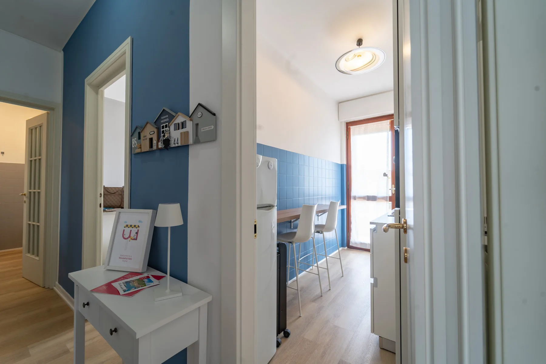 A blue-walled hallway opens onto a bright dining area with a table and chairs.