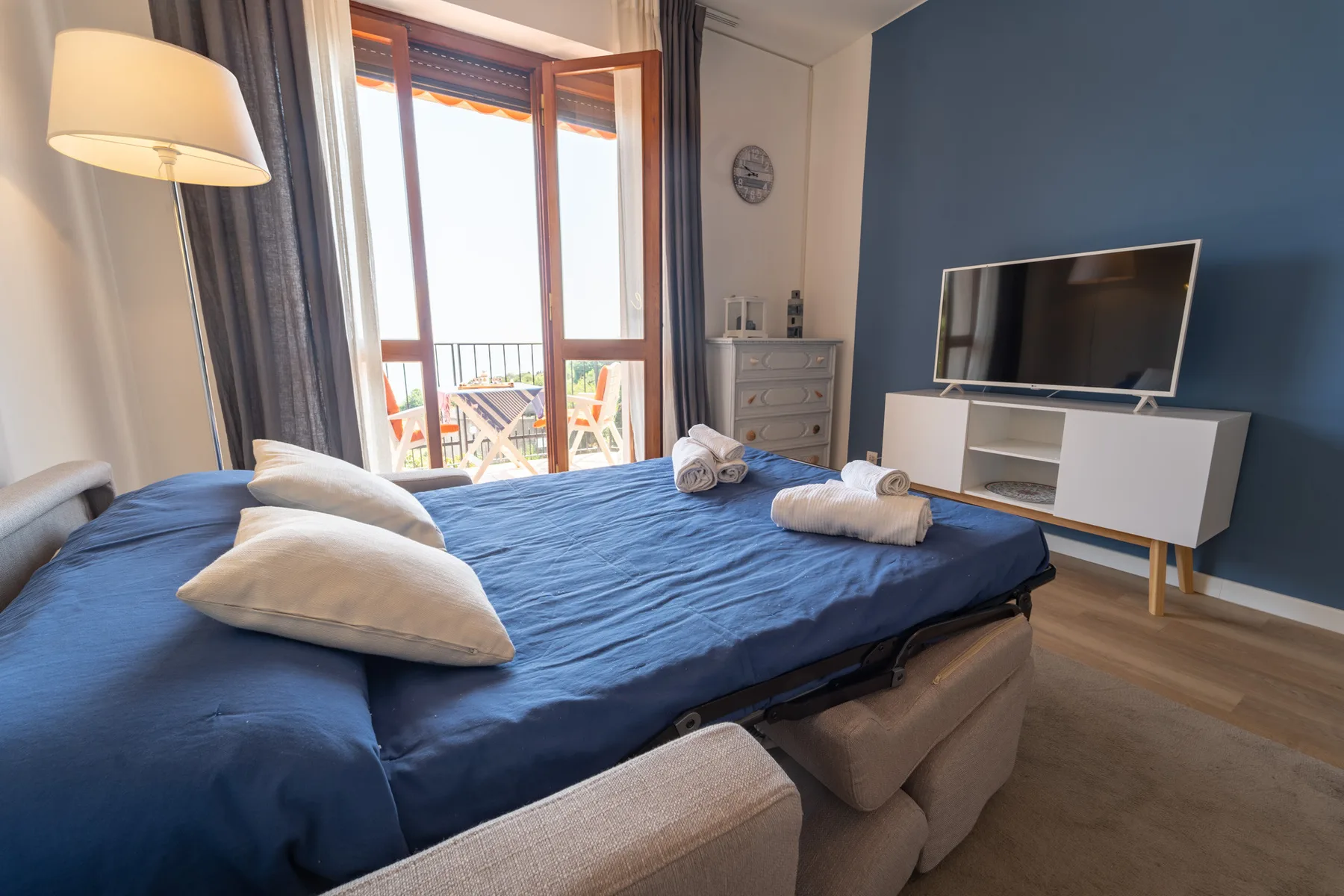 A bedroom with a blue-covered bed facing a television on a low cabinet.