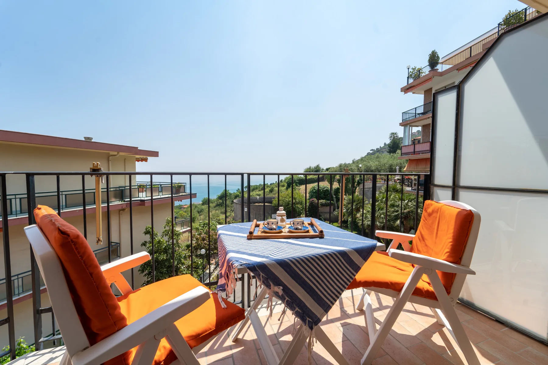 An outdoor balcony seating area with a table overlooking nearby buildings and greenery.