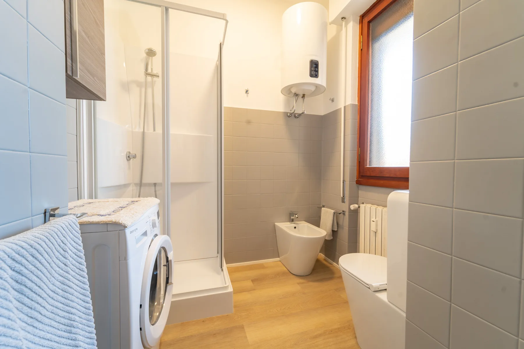 A tiled bathroom with a shower, toilet, and washing machine.
