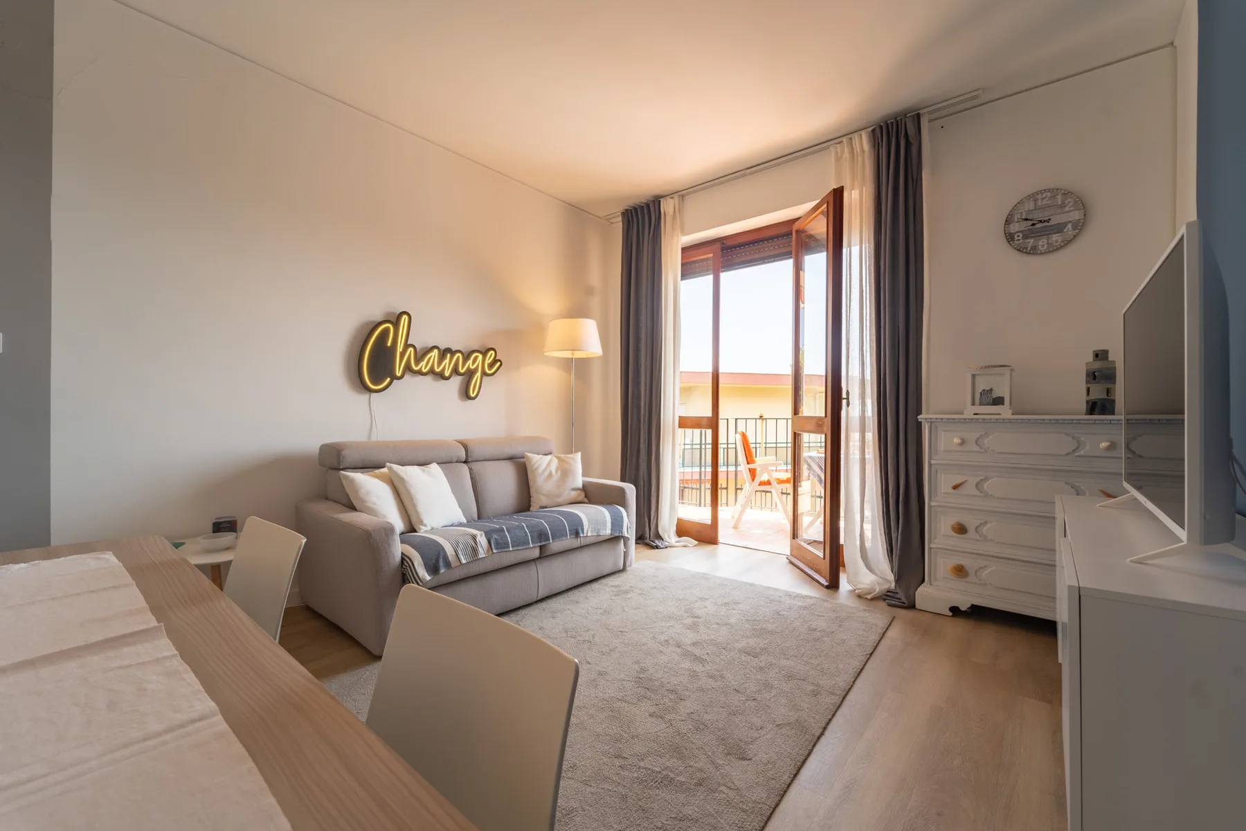 A bright living room with a sofa, dining table, and open balcony doors.