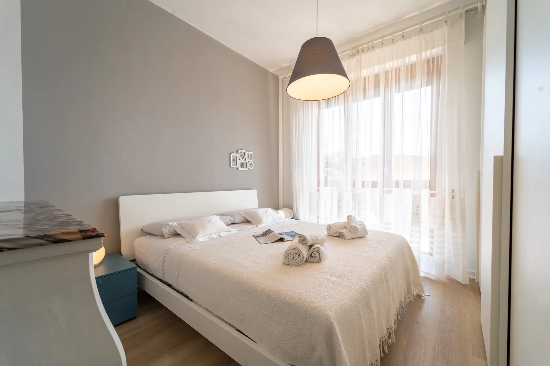A bright bedroom with a neatly made bed beside sheer curtains.