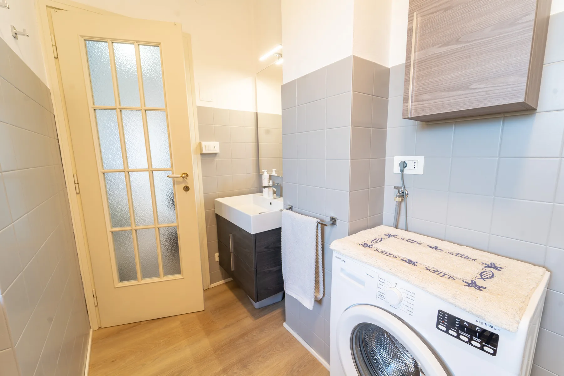 A compact bathroom with a sink, washing machine, and frosted-glass door.