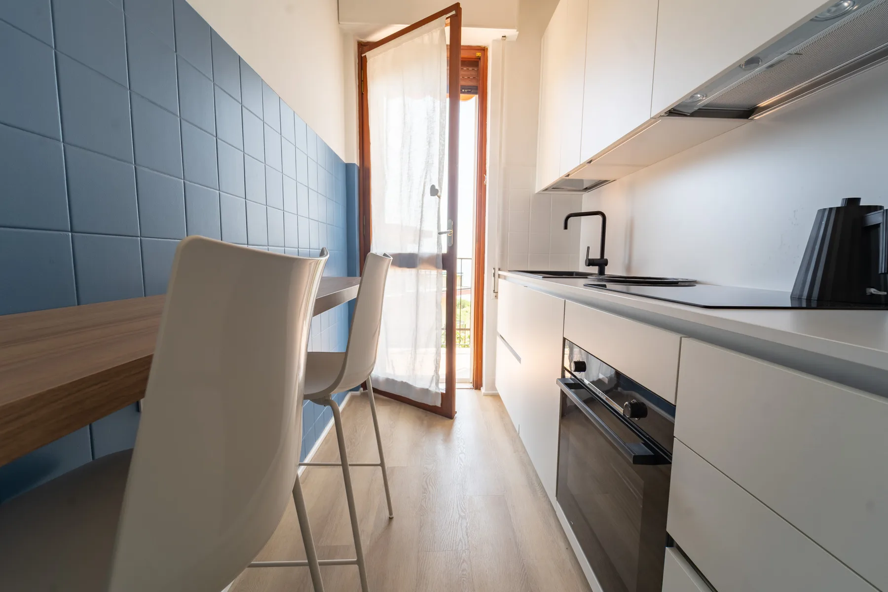 A narrow modern kitchen with a dining table and chairs beside the counter.