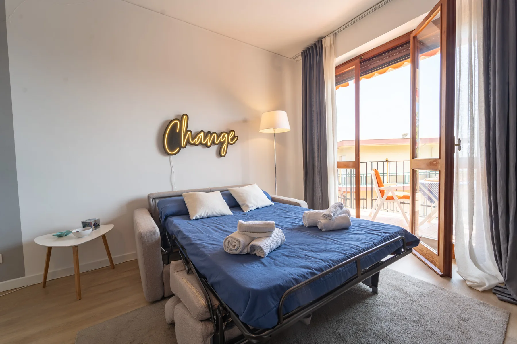 A bedroom with a bed dressed in blue bedding beside an open balcony door.