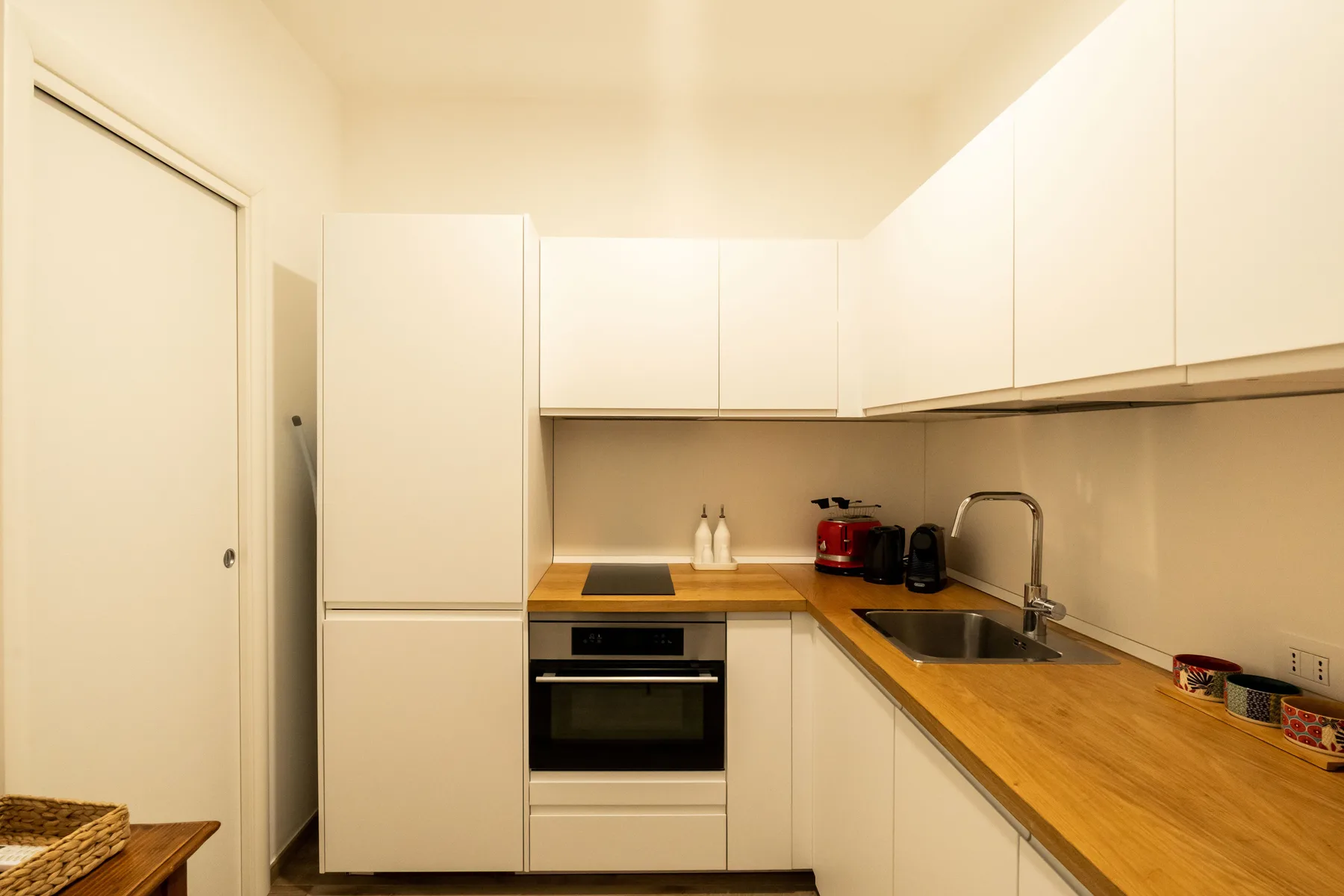 A compact kitchen with white cabinets, a built-in oven, and wooden countertops.
