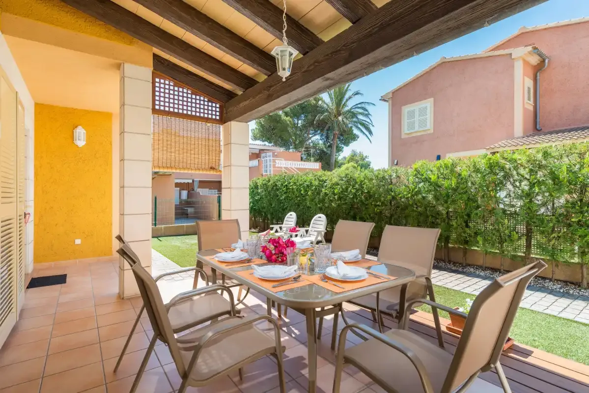 A covered patio with an outdoor dining table and seating beside a hedge.