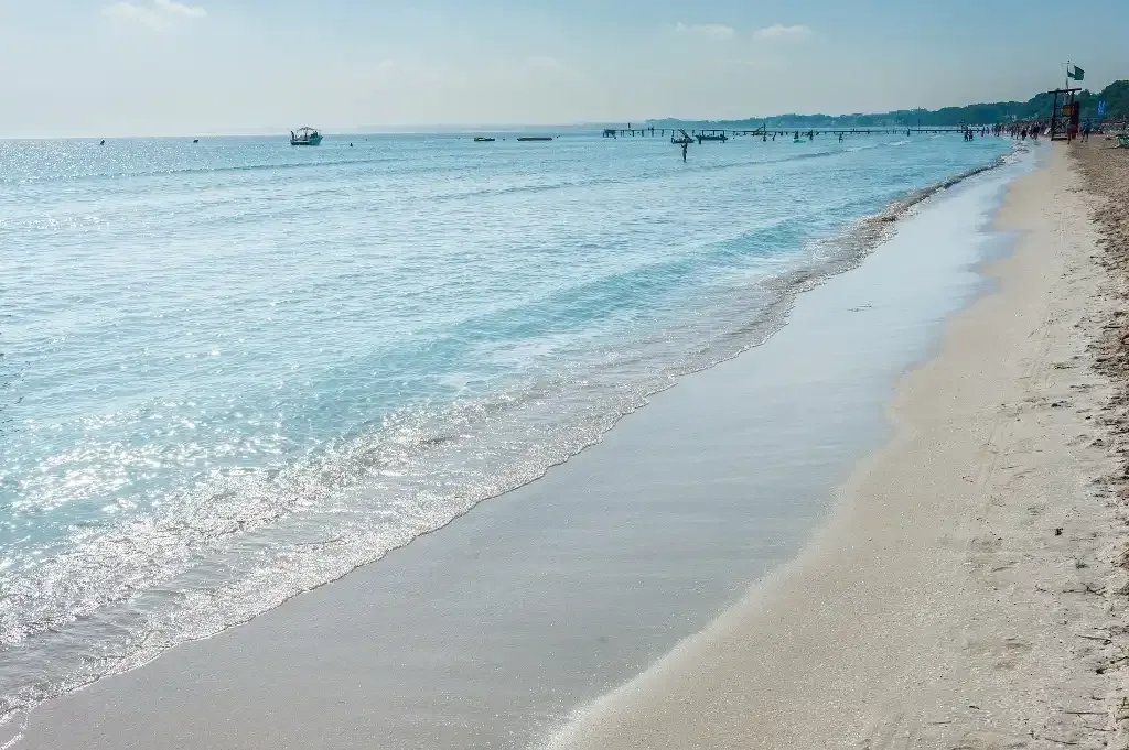 A sandy beach meets clear blue water beneath a bright sky.