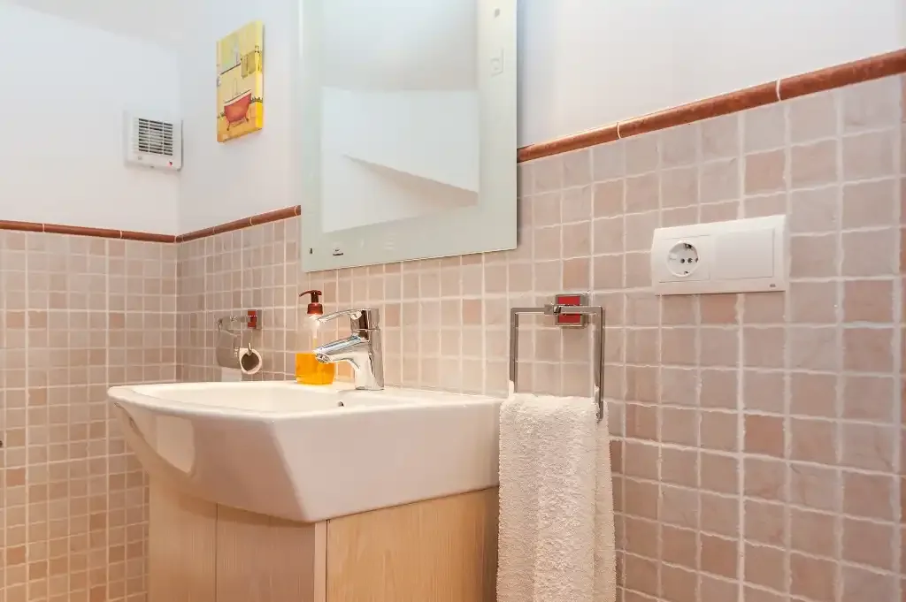 A bathroom with a wall-mounted sink and tiled walls.