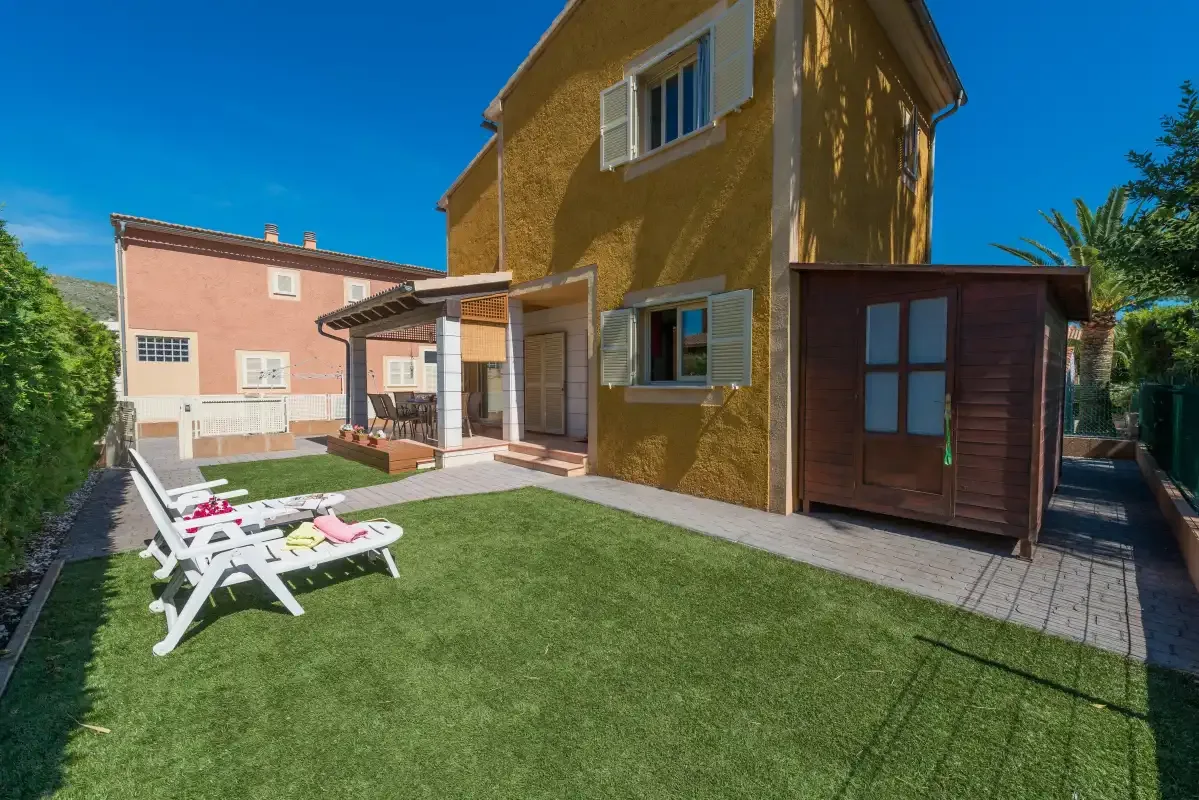 A two-story house overlooks a lawn with outdoor seating and a shaded patio.