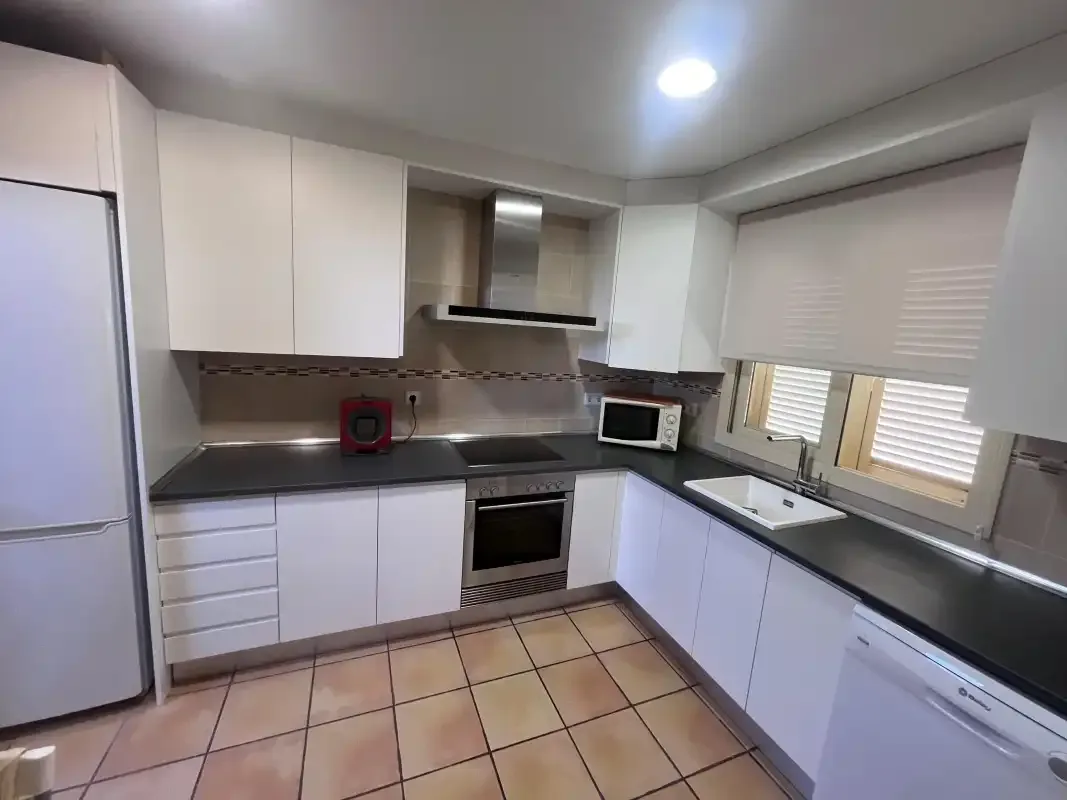 A modern kitchen with white cabinets, dark countertops, and built-in appliances.