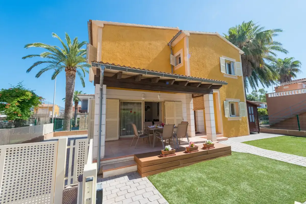 A yellow house opens onto a patio with outdoor seating and a lawn.