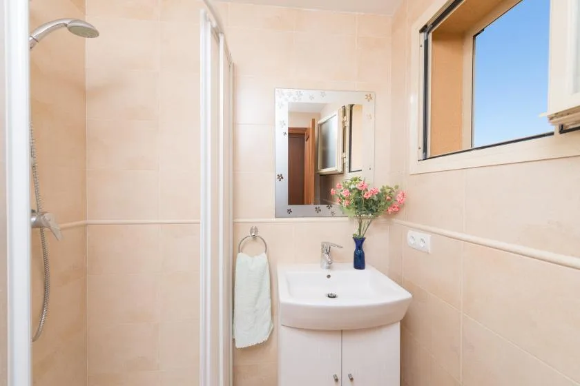 A bathroom with a wall-mounted sink, mirror, and window.