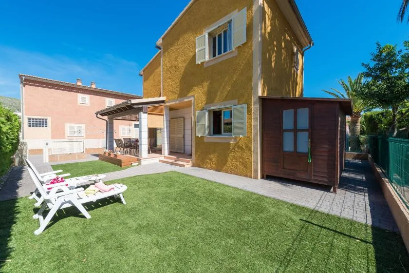 A sunny yard beside a yellow house, with lawn and outdoor seating.