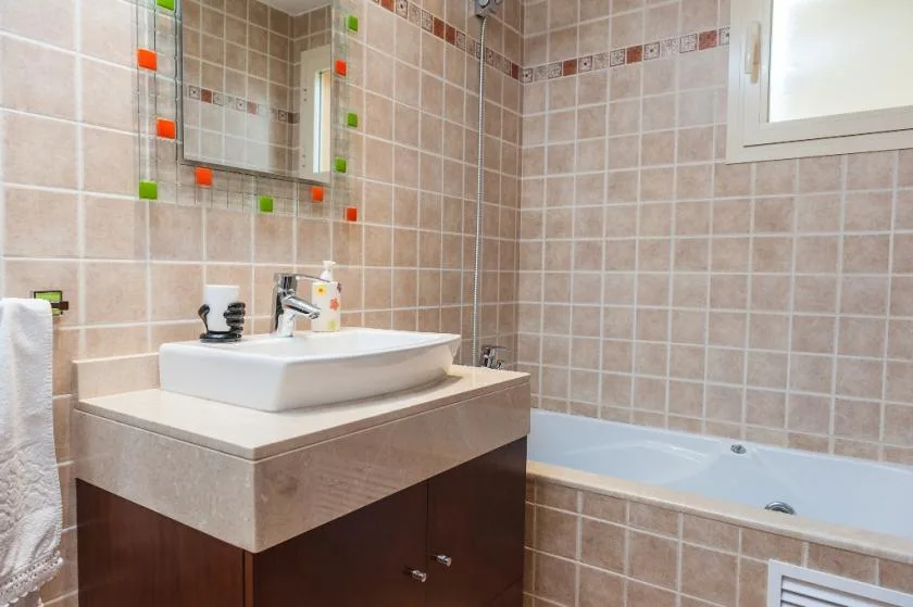 A tiled bathroom with a sink vanity, bathtub, and window.