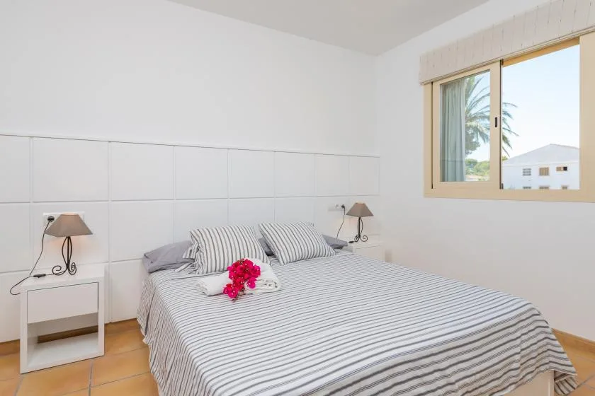 A bedroom with striped bedding and a window overlooking nearby buildings.
