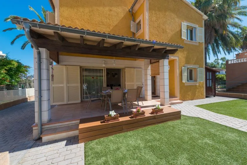 A yellow house opens onto a paved patio with a covered seating area and lawn.