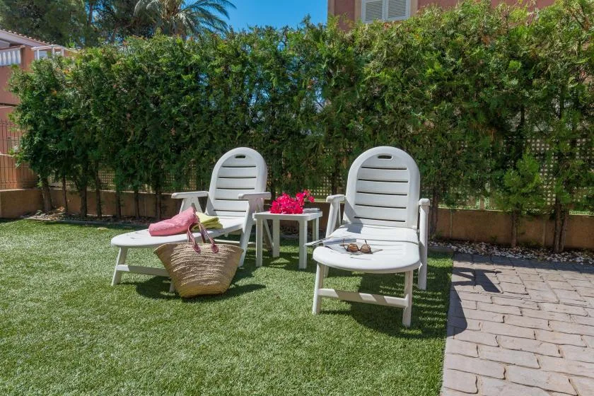 Outdoor seating on a lawn beside a paved path and leafy hedge.