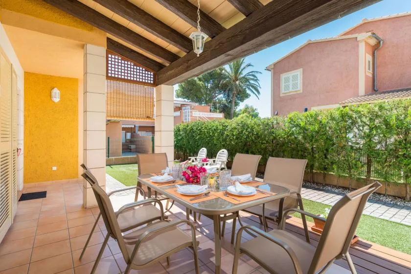 A covered outdoor dining area with a table and chairs beside a garden hedge.