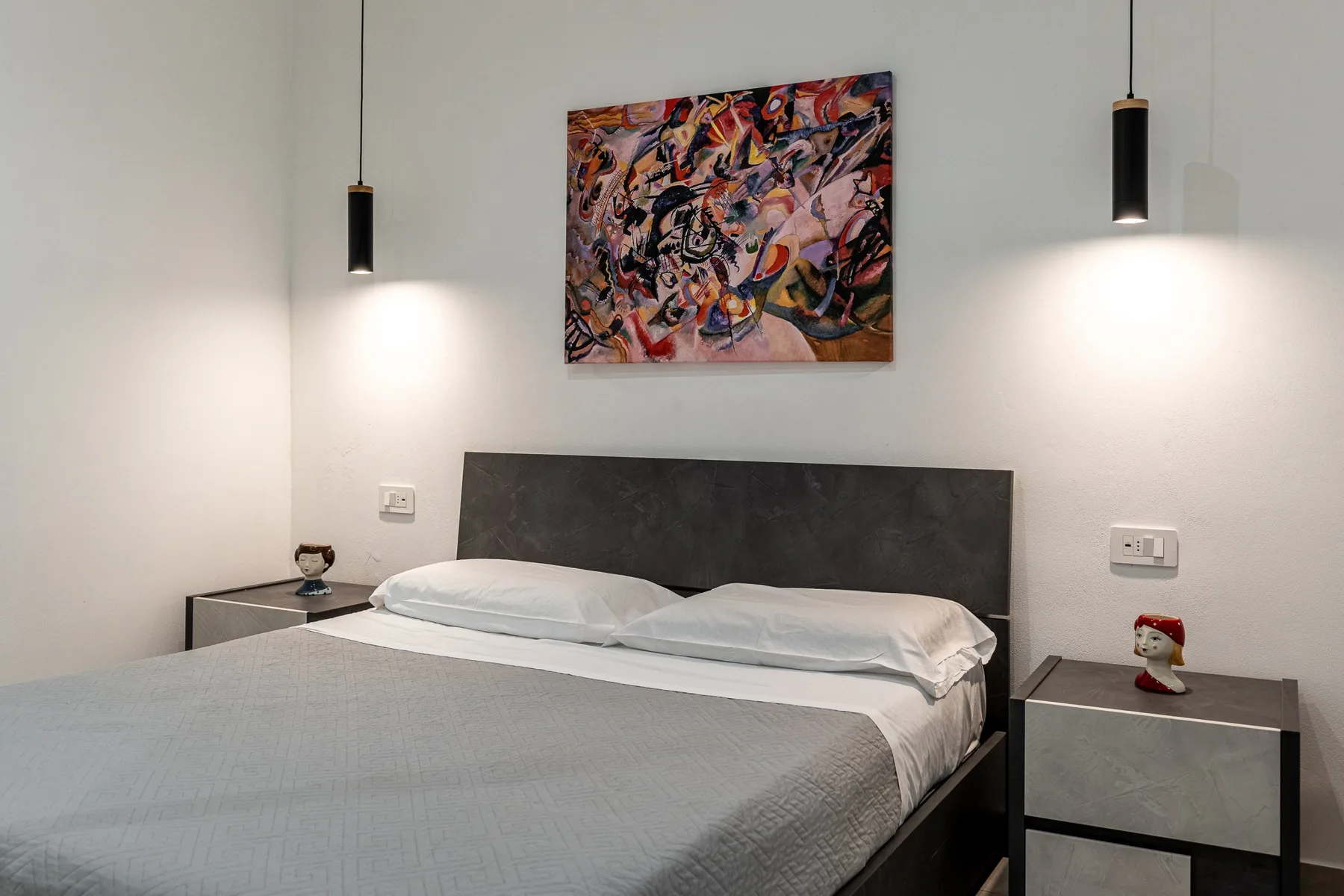 A bedroom with a bed, two bedside tables, and colorful artwork above the headboard.