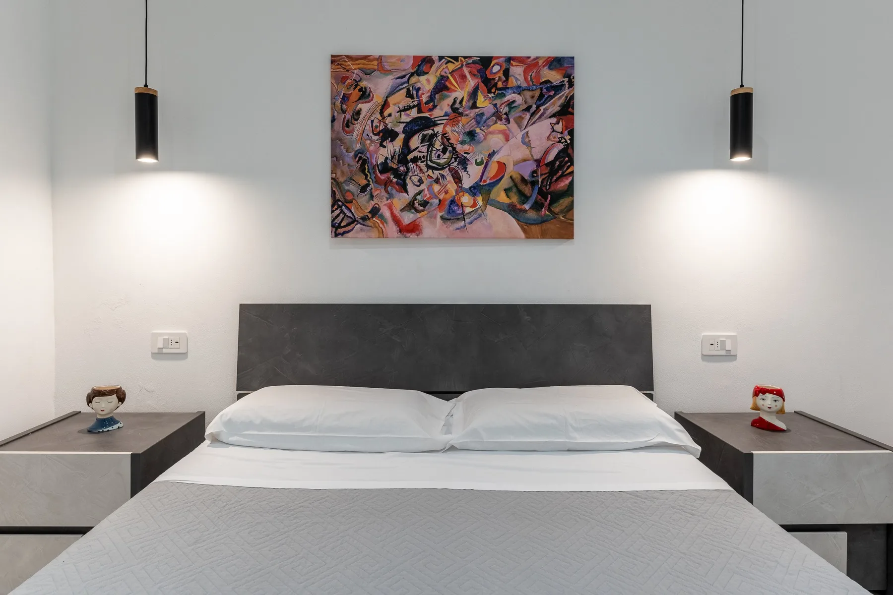 Un dormitorio con una cama doble, una obra abstracta y mesitas de noche a juego.
