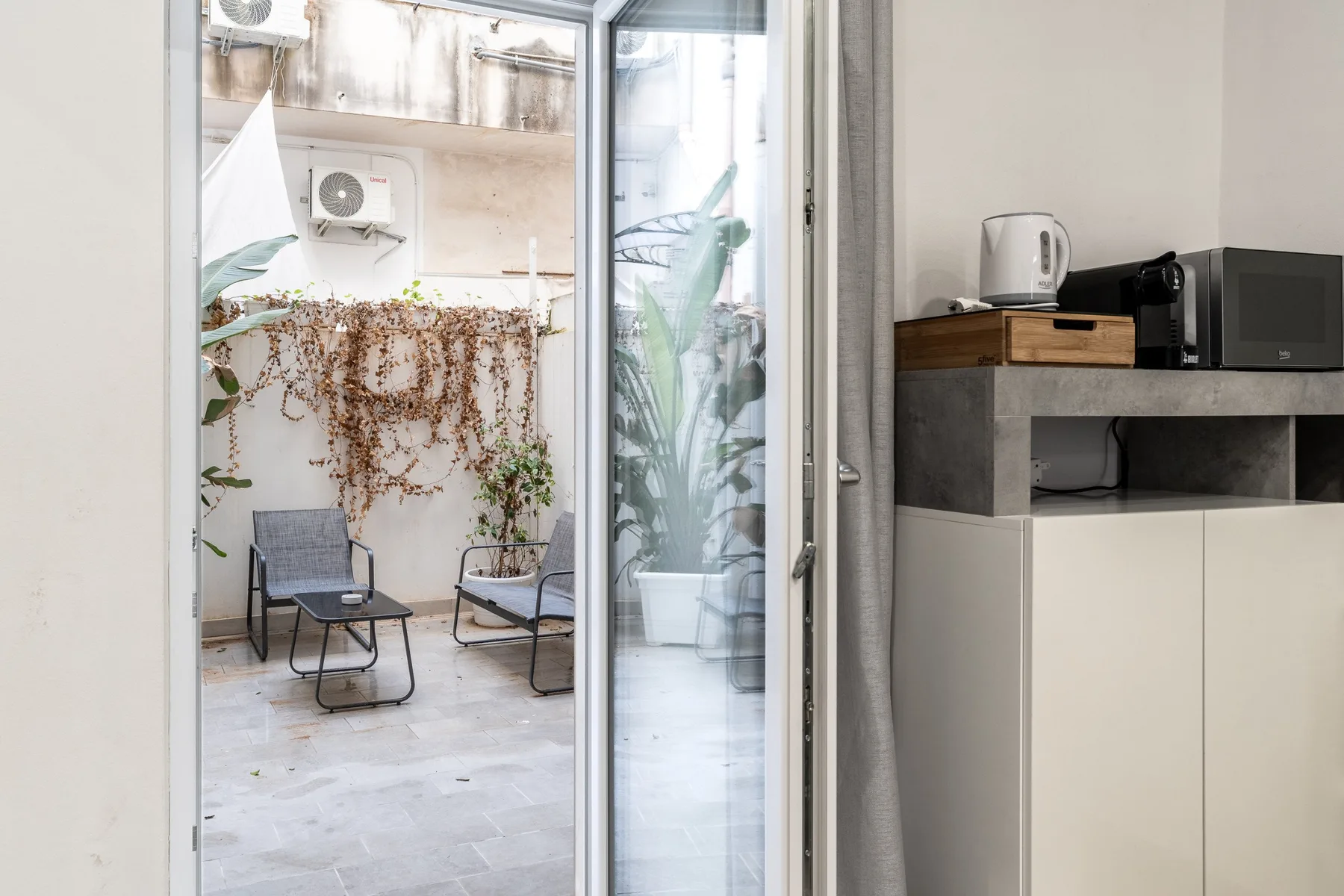 A small kitchenette beside a glass door opening onto a plant-filled patio.