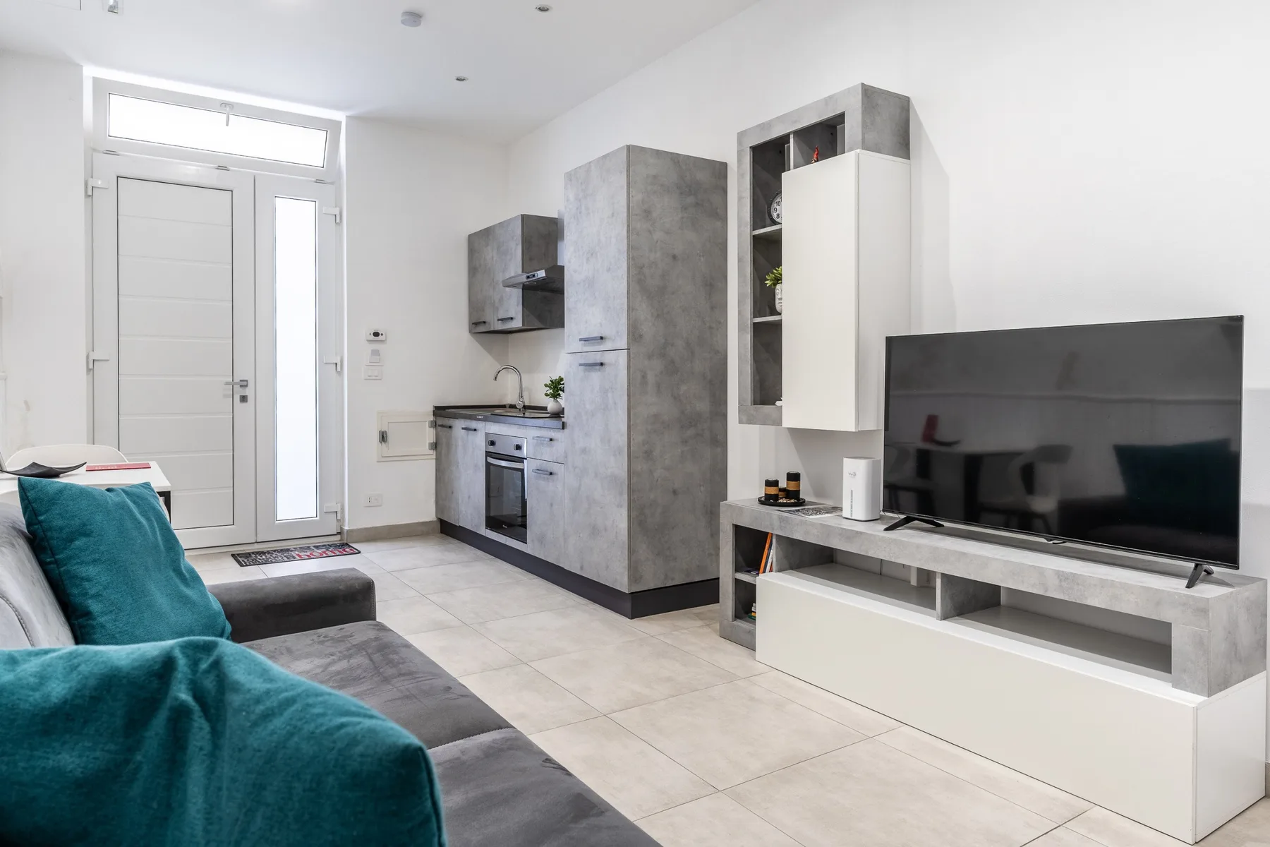Una sala de estar moderna con asientos, un televisor y una cocina compacta.