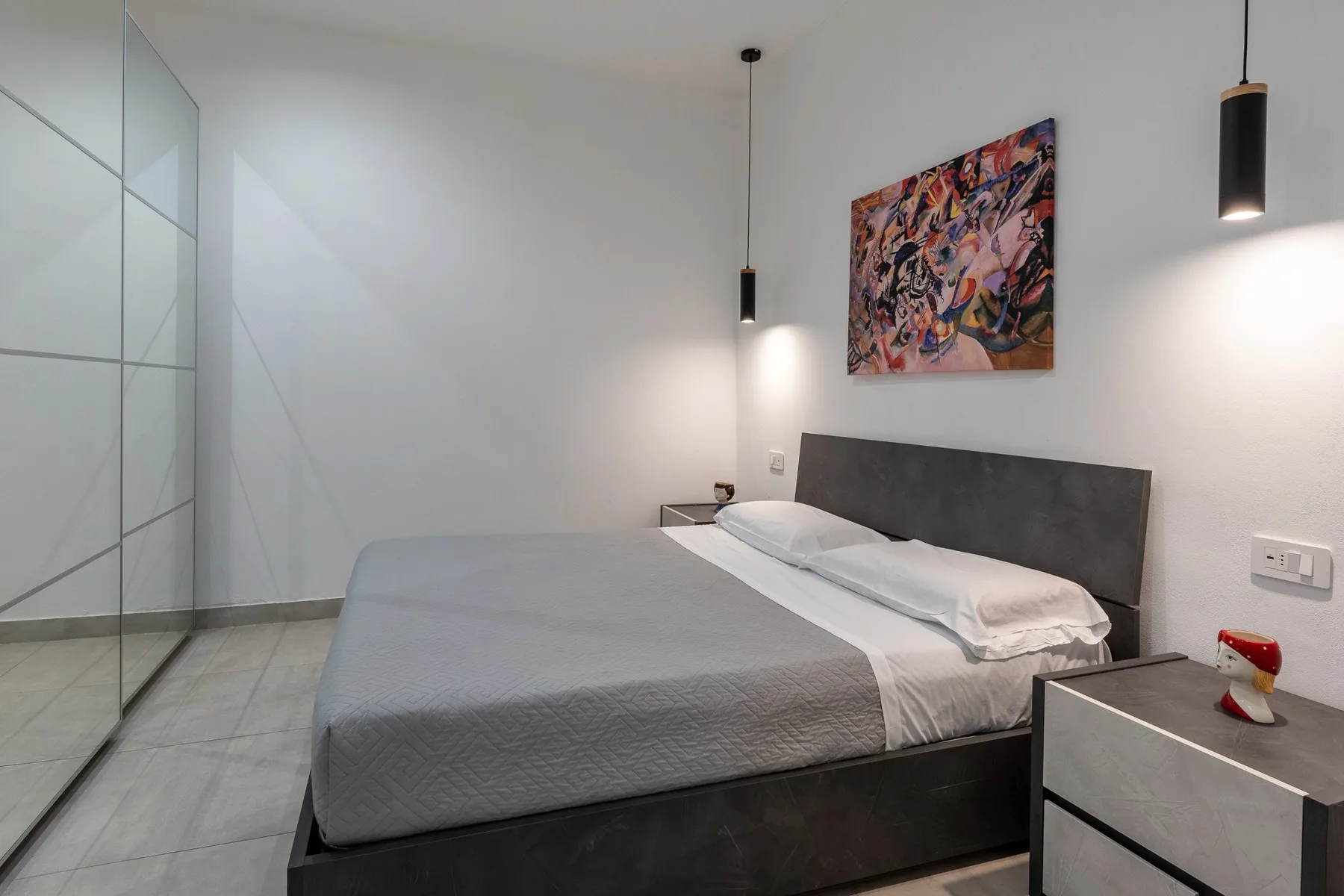 A modern bedroom with a neatly made bed and colorful artwork on the wall.