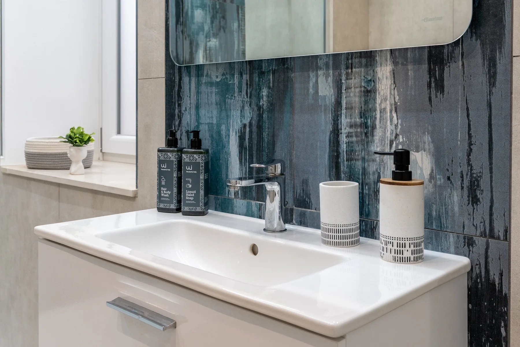 A bathroom vanity with a white sink, toiletries, and a large mirror.