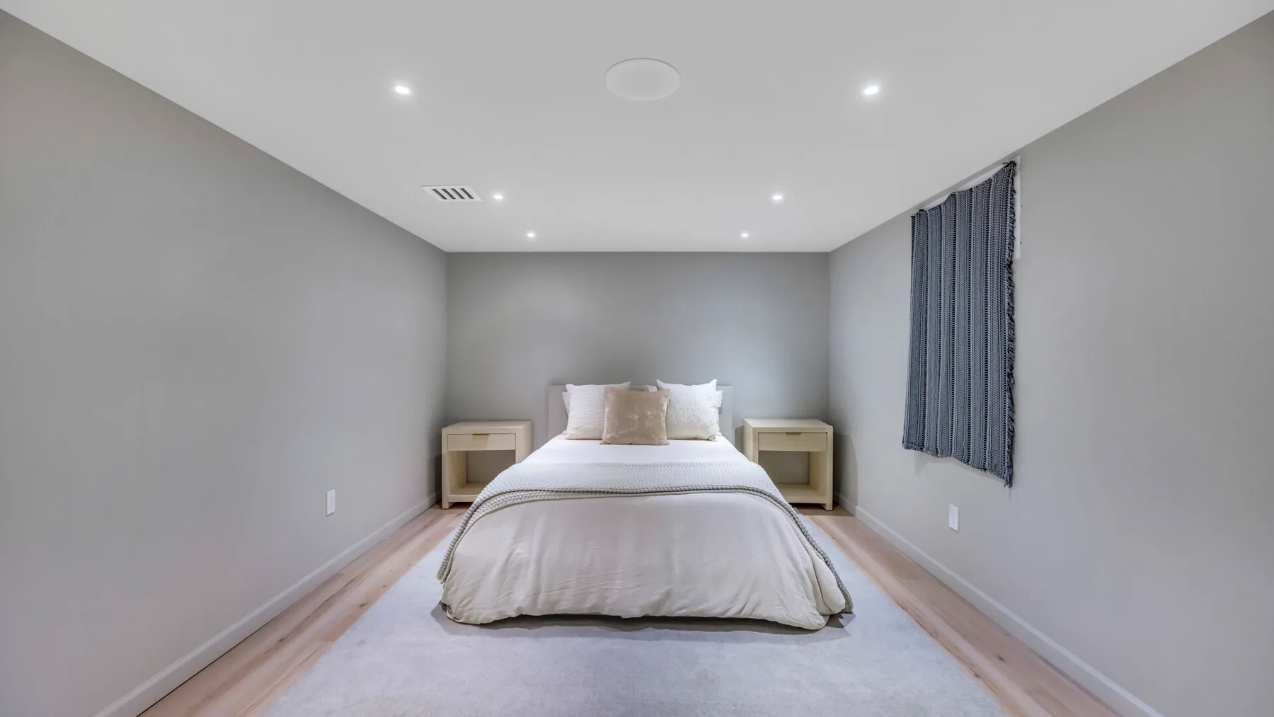 A bedroom with a bed centered against the back wall and a window with curtains.
