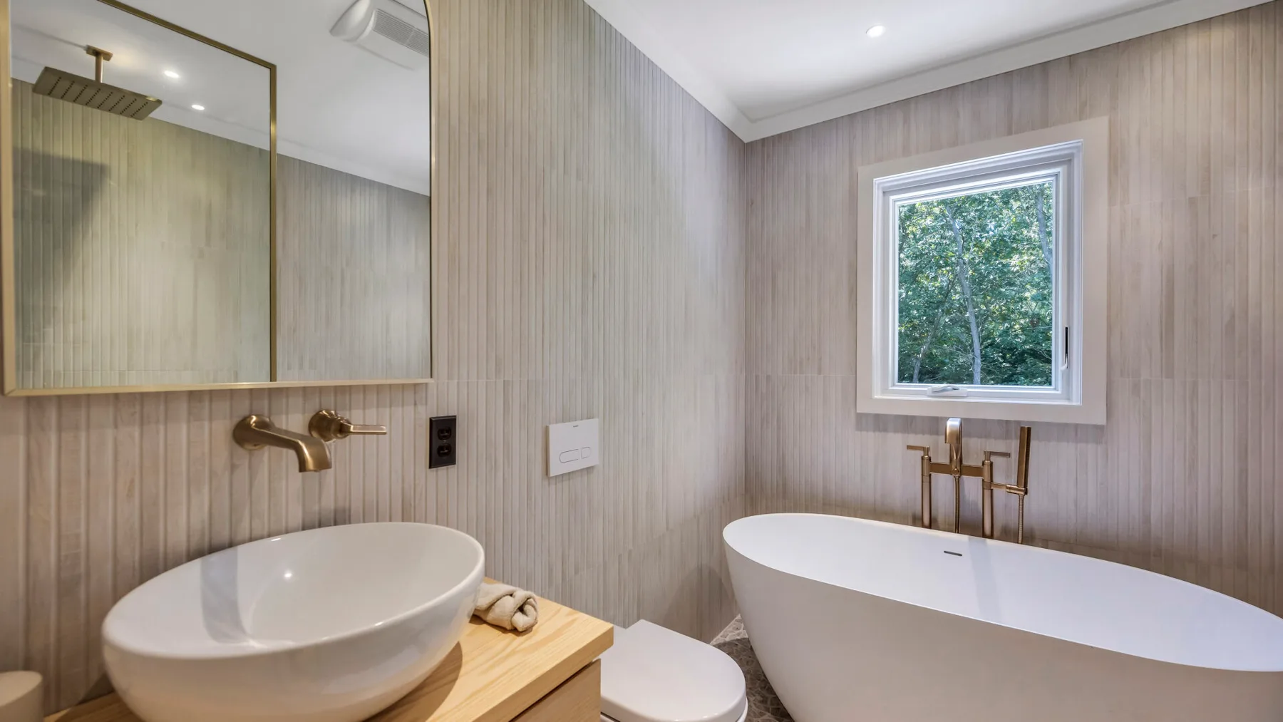 A bathroom with a freestanding tub, vanity sink, and window.