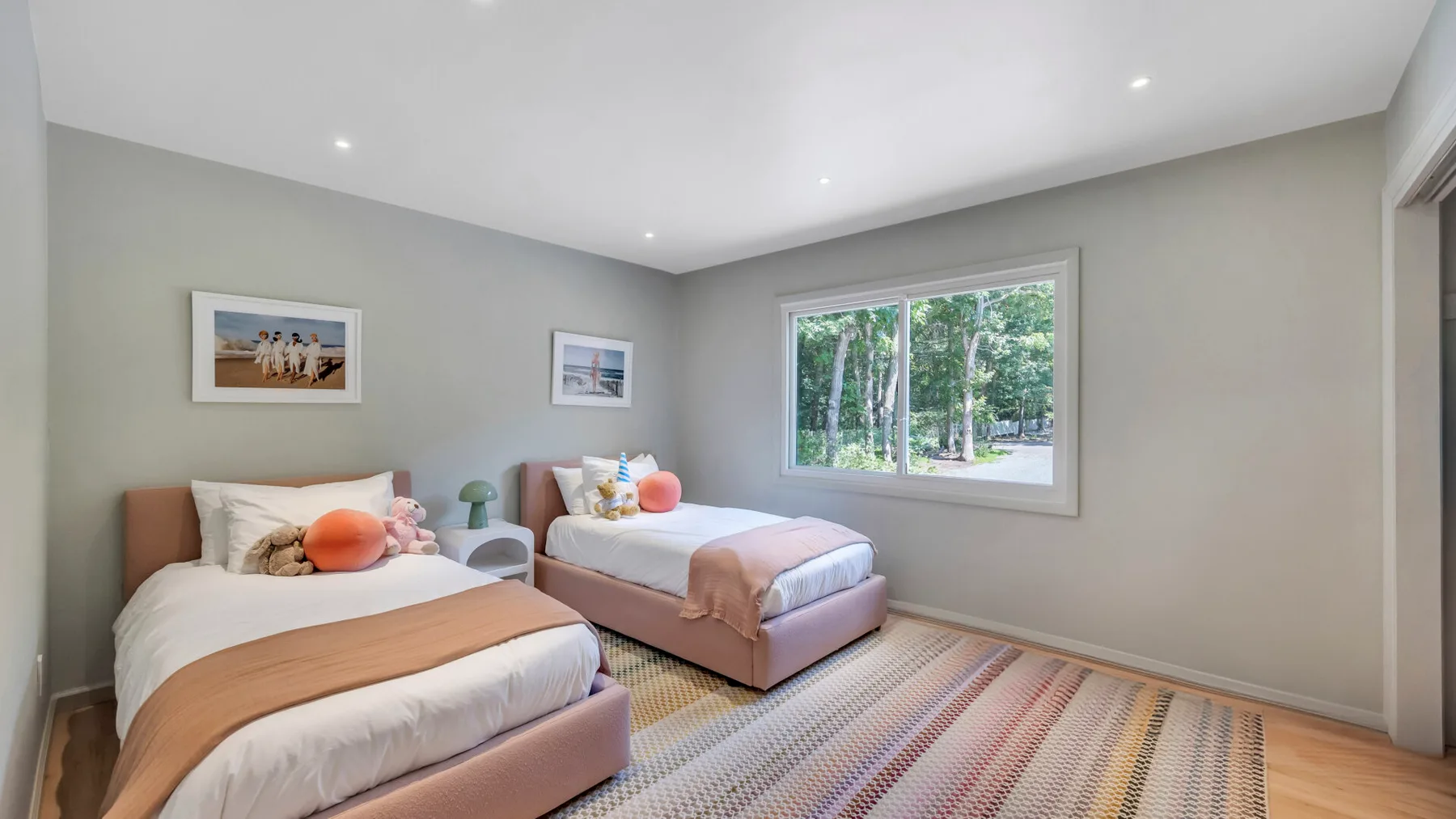 A bright bedroom with two beds and a large window overlooking trees.