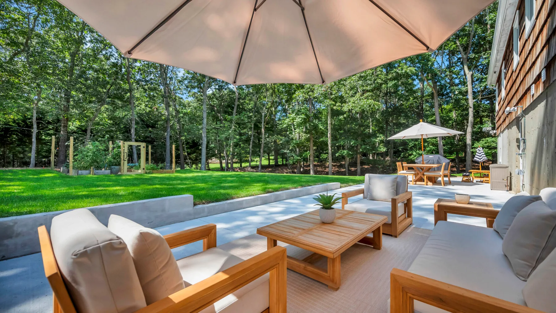 A patio seating area faces a green lawn and surrounding trees.