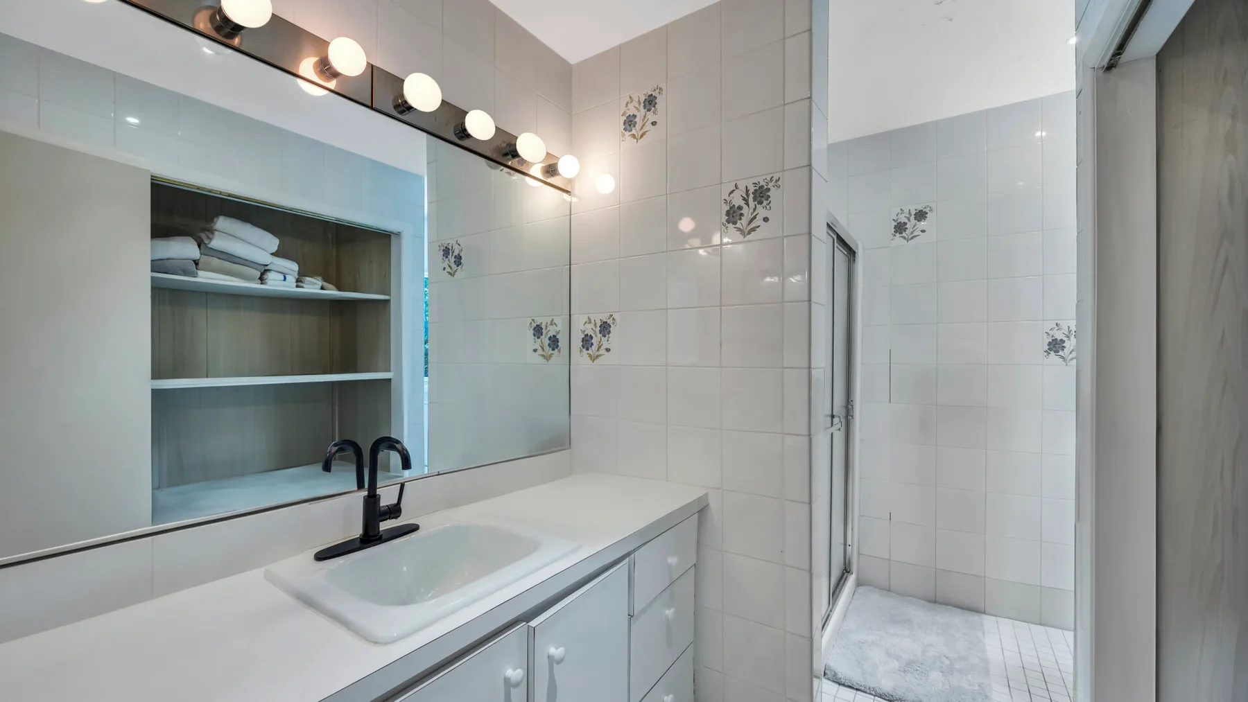 A tiled bathroom vanity with a wide mirror and an adjoining shower.