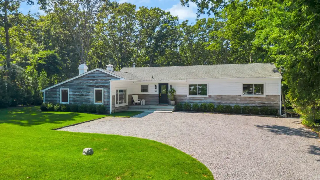 A single-story house sits beside a curved gravel driveway and green lawn.