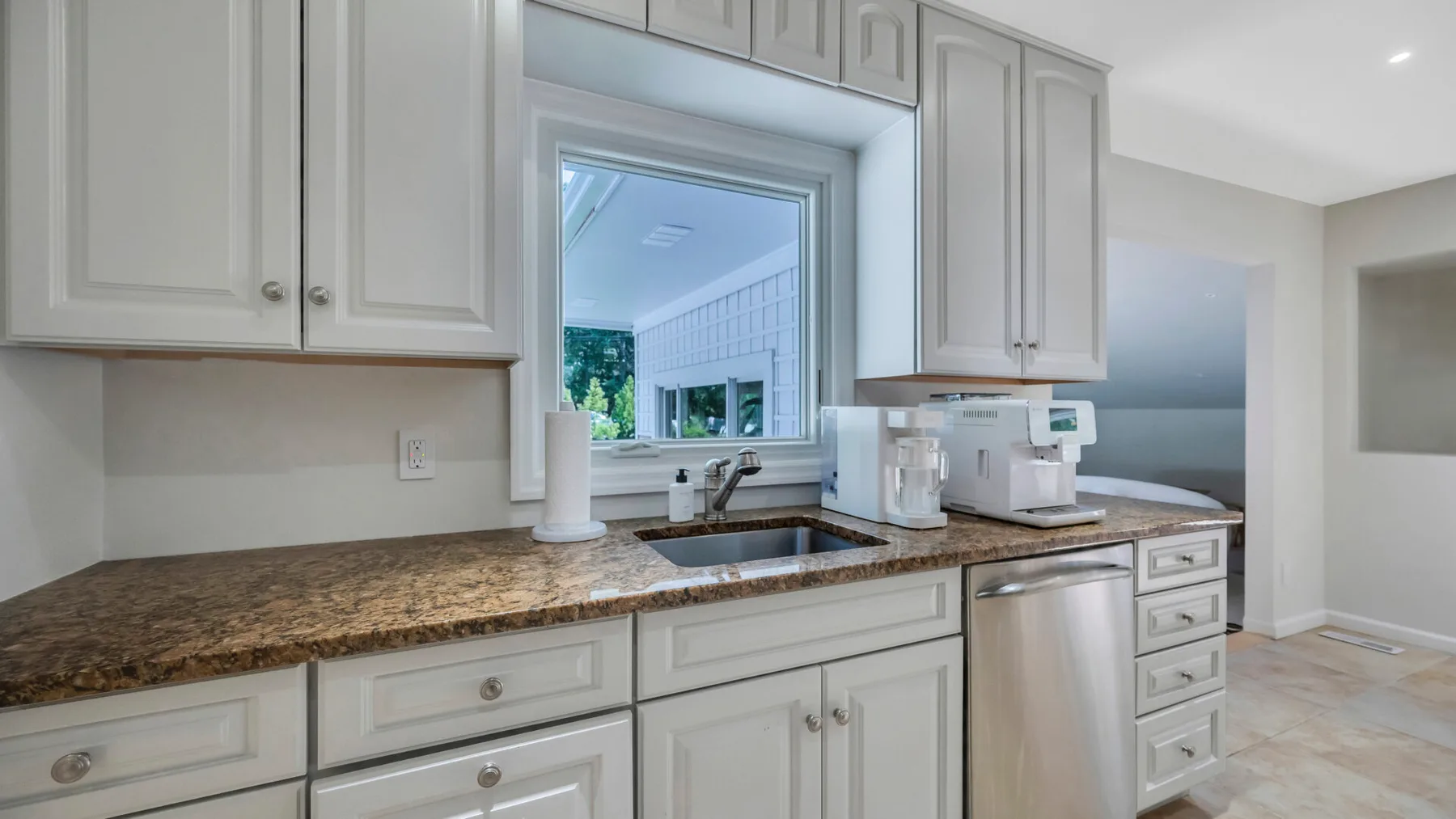 A bright kitchen with white cabinets, a sink, and a countertop.
