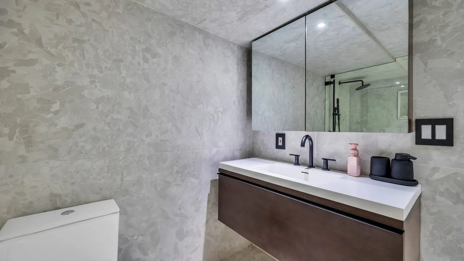 A modern bathroom vanity with a wide mirror and a shower in the background.