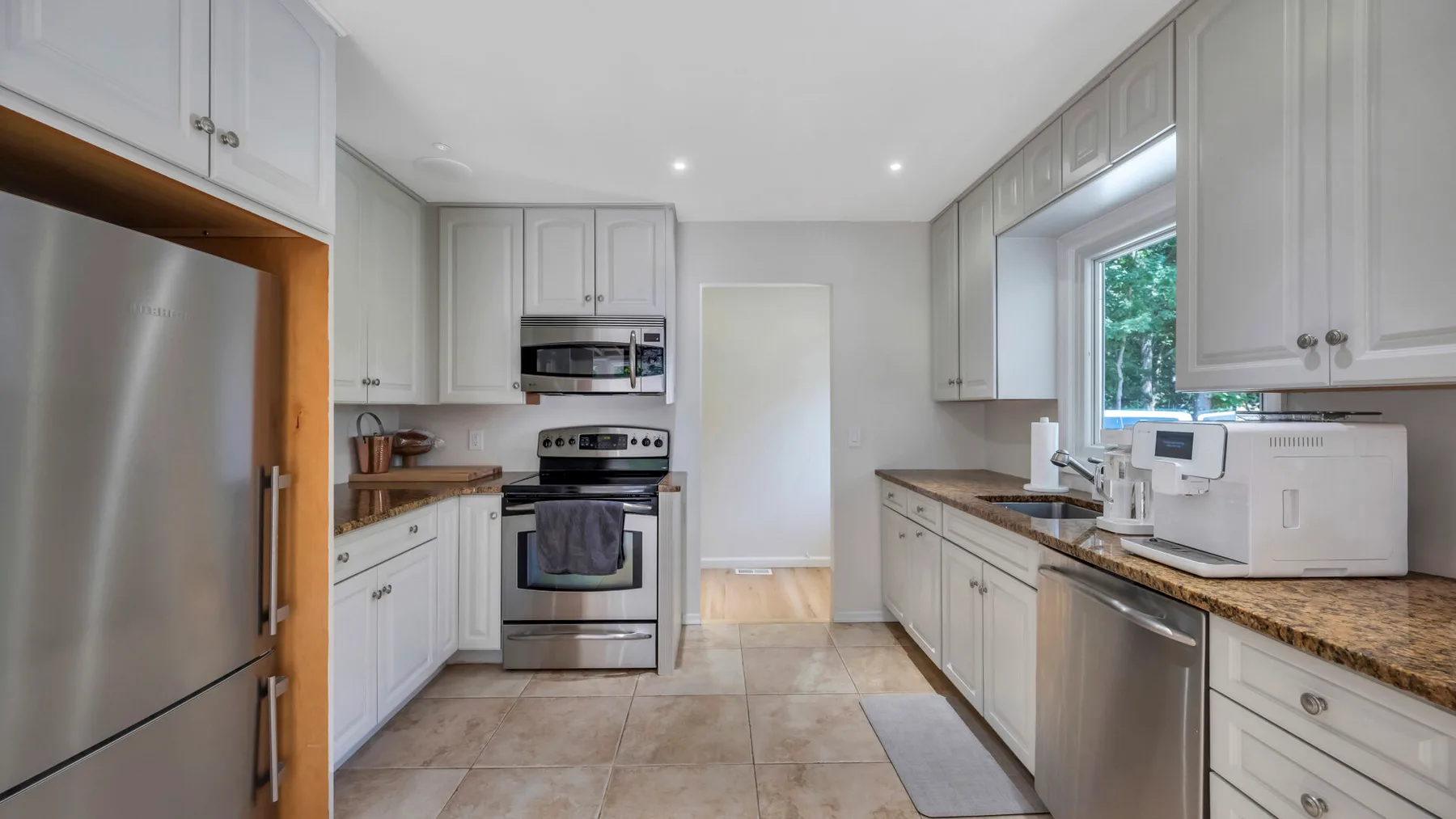 A bright kitchen with white cabinets, stainless steel appliances, and a window.