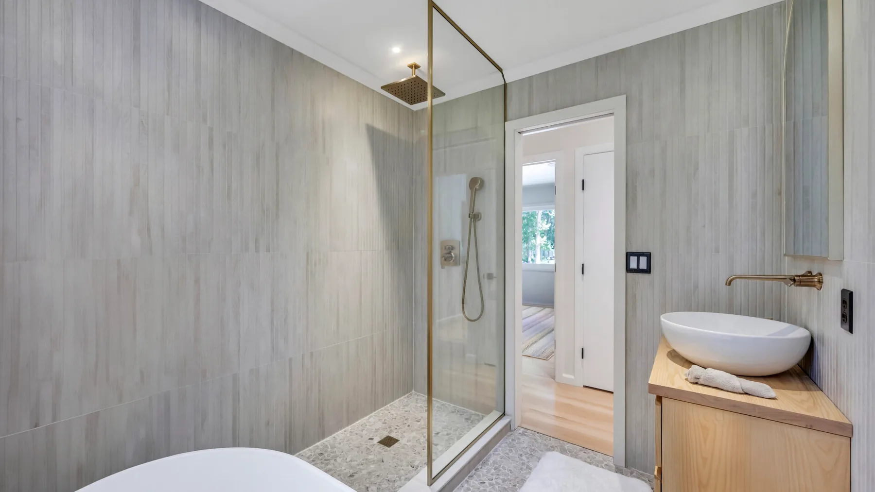 A bright bathroom with a glass shower and a vessel sink on a wooden vanity.