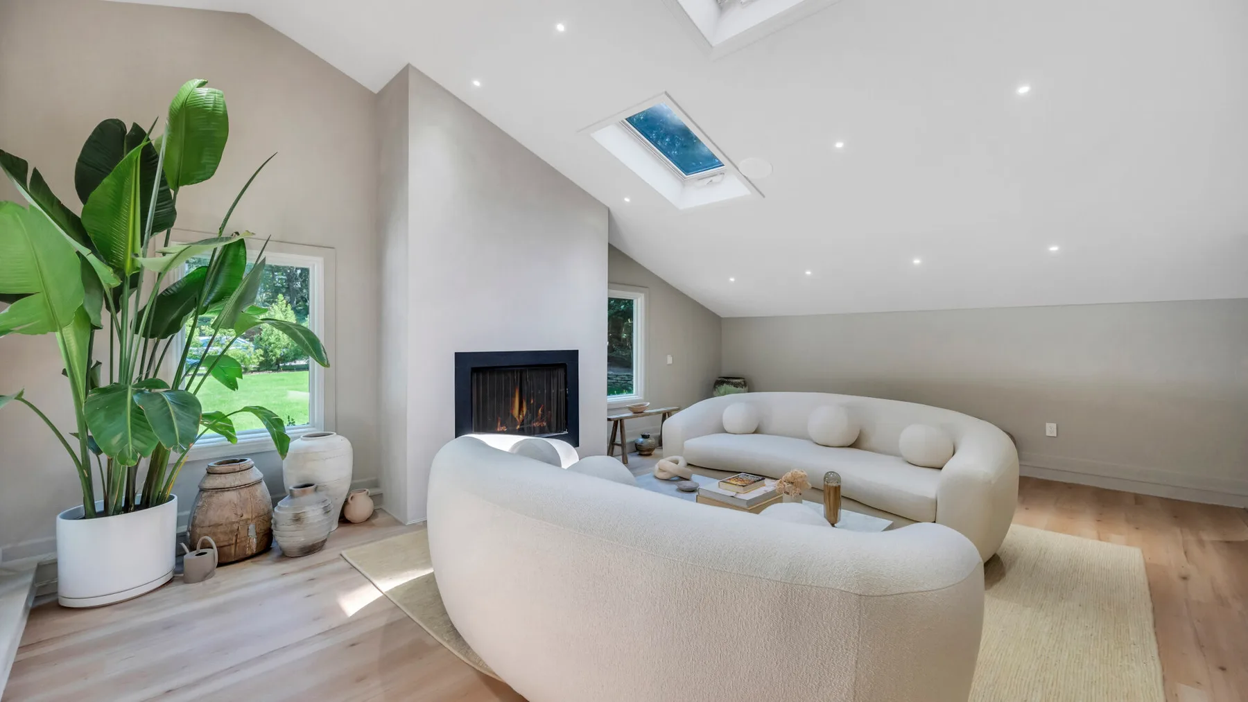 A bright living room with curved seating, a fireplace, and large potted plants.