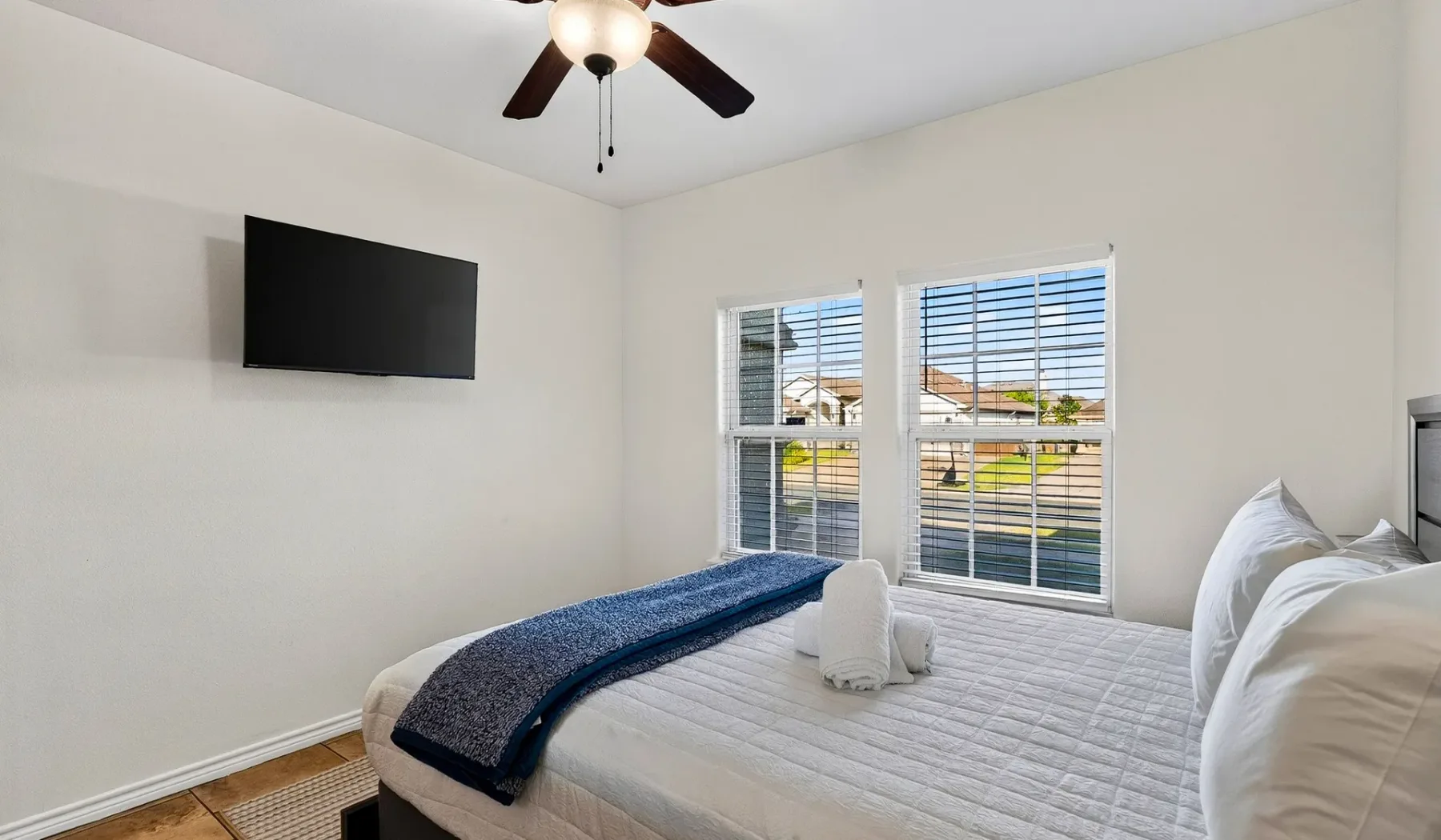 Un dormitorio con una cama, un televisor en la pared y ventanas con persianas.
